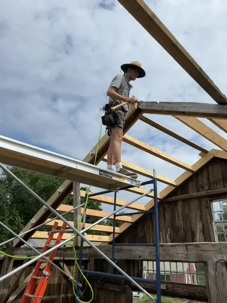 Dave on scaffolding framing the barn roof against an open summer sky